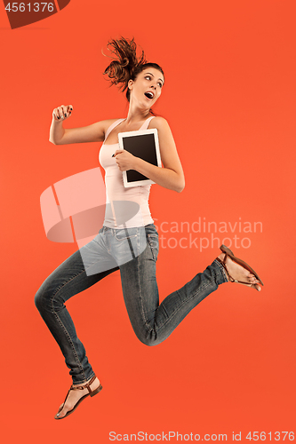 Image of Image of young woman over blue background using laptop computer or tablet gadget while jumping.