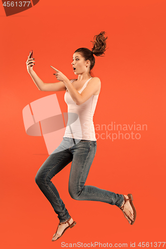 Image of Image of young woman over blue background using laptop computer or tablet gadget while jumping.