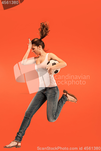 Image of Forward to the victory.The young woman as soccer football player jumping and kicking the ball at studio on a red