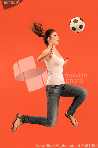 Image of Forward to the victory.The young woman as soccer football player jumping and kicking the ball at studio on a red