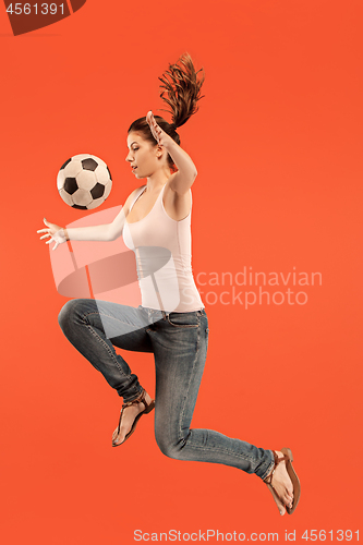 Image of Forward to the victory.The young woman as soccer football player jumping and kicking the ball at studio on a red