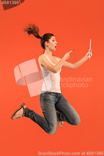 Image of Image of young woman over blue background using laptop computer or tablet gadget while jumping.