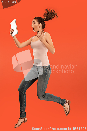 Image of Image of young woman over blue background using laptop computer or tablet gadget while jumping.