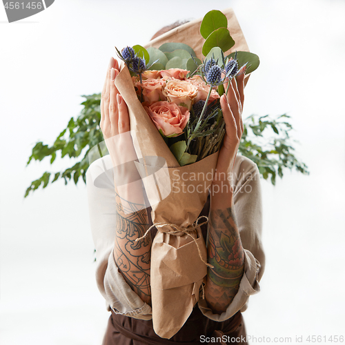 Image of Wonderful bouquet from coral color roses and eryngium in girl\'s hands on a light background with green leaf. Copy space. Greeting post card.