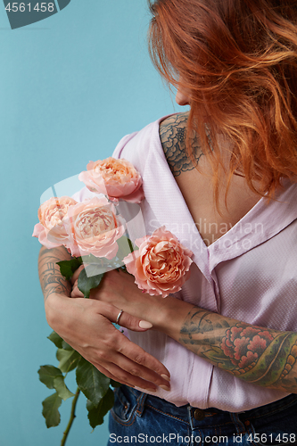 Image of A girl with a tattoo on her hand holds delicate pink roses around a blue background with space for text. Valentine\'s Day Gift