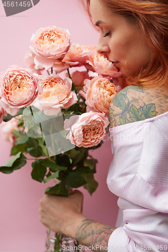 Image of Pretty woman with ginger hair, tattoo on her shoulder and hands, holds bouquet of roses on a living coral background. Card on Woman\'s or Mother\'s Day.