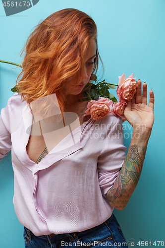Image of Sexual girl with ginger hair and flowers living coral color in her hands with tattoo on a blue background, copy space. Gift on Woman\'s, Mother\'s Day.