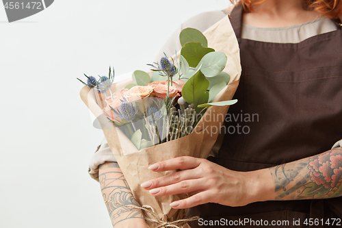 Image of Fresh flowers living coral roses and eryngium as a congratulate bouquet in girl\'s hand with tattoo, copy space. Post card for Mother\'s Day.