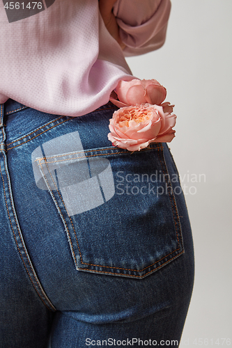 Image of Woman wearing of jean pants and pink shirt from back with fresh flowers in a pocket on a gray background, copy space.
