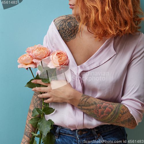 Image of A young woman with a tattoo holds in her hand a bouquet of pink roses around a blue background with copy space. Mother\'s day concept