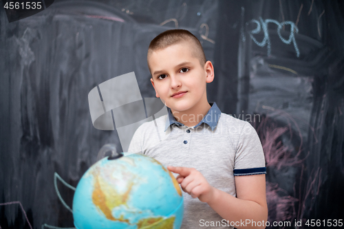 Image of boy using globe of earth in front of chalkboard