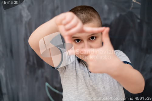 Image of happy boy making hand frame gesture in front of chalkboard