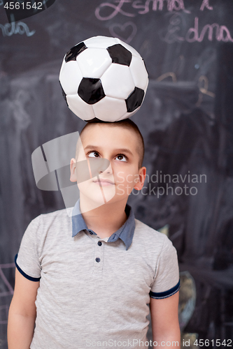 Image of happy boy holding a soccer ball on his head