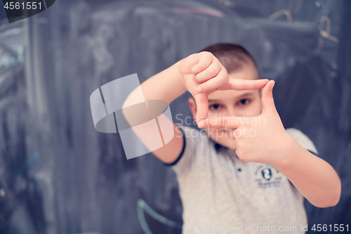 Image of happy boy making hand frame gesture in front of chalkboard