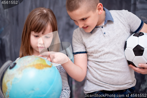 Image of boy and little girl using globe of earth in front of chalkboard