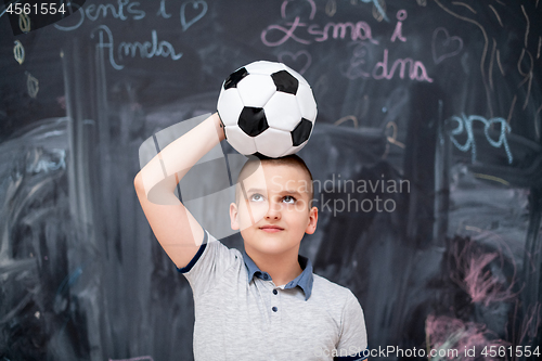 Image of happy boy holding a soccer ball on his head