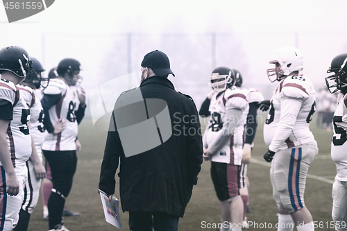 Image of american football players discussing strategy with coach