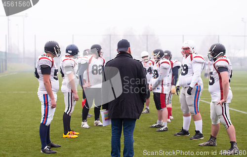 Image of american football players discussing strategy with coach