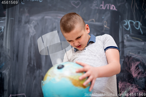 Image of boy using globe of earth in front of chalkboard