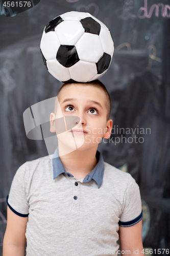 Image of happy boy holding a soccer ball on his head