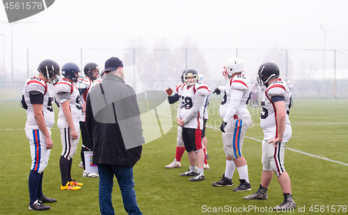 Image of american football players discussing strategy with coach