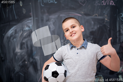 Image of happy boy holding a soccer ball in front of chalkboard