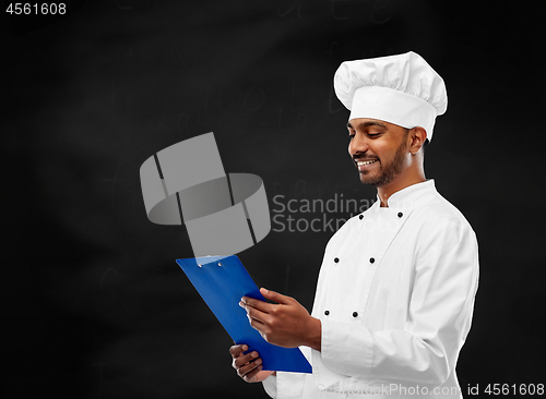 Image of chef reading menu on clipboard over chalkboard