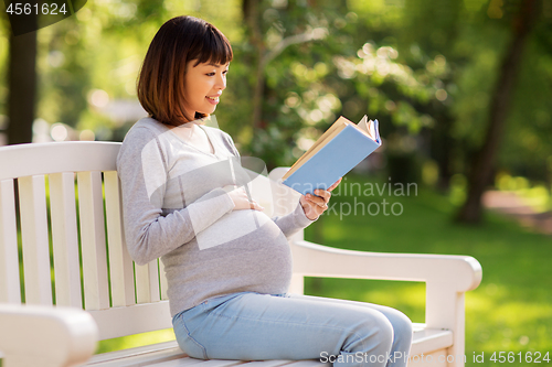 Image of happy pregnant asian woman reading book at park