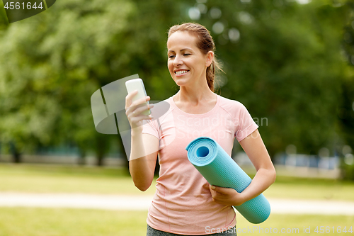 Image of woman with exercise mat and smartphone at park