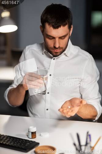 Image of businessman taking medicine pills at night office