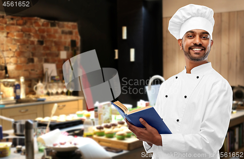 Image of happy male indian chef with cookbook at kitchen