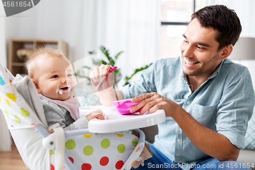 Image of father feeding happy baby in highchair at home