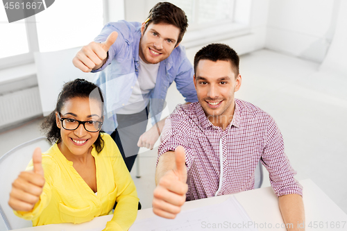 Image of happy creative team showing thumbs up at office