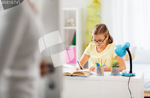 Image of schoolgirl doing homework and mother entering room