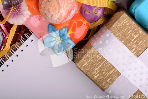 Image of Arrangement of Gift Boxes in Wrapping Paper with Checkered Ribbons and Decorated Easter Eggs. White paper notepad