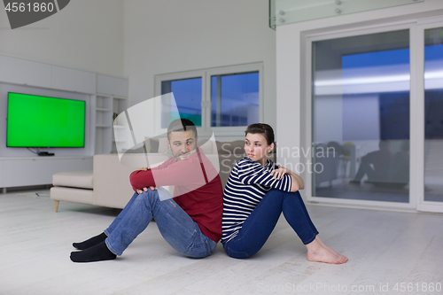 Image of young couple sitting with back to each other on floor