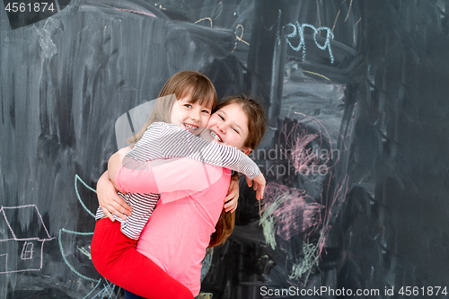 Image of little girls hugging in front of chalkboard