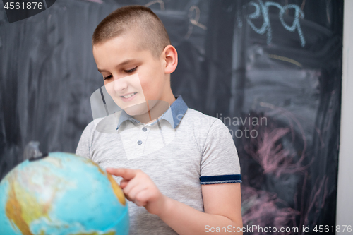 Image of boy using globe of earth in front of chalkboard