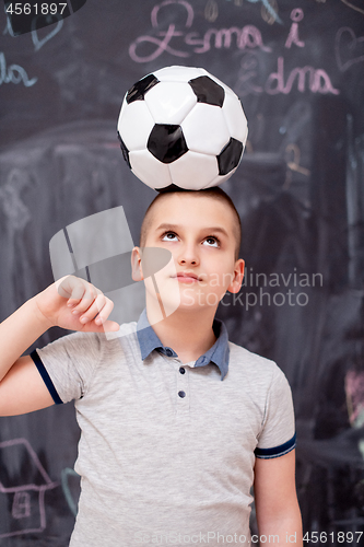 Image of happy boy holding a soccer ball on his head