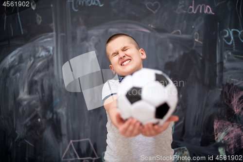 Image of happy boy holding a soccer ball in front of chalkboard