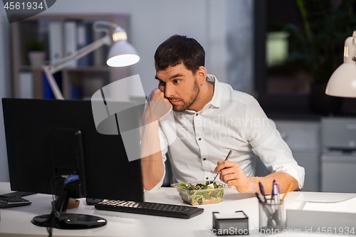 Image of businessman with computer eating at night office