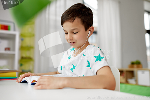 Image of student boy in earphones reading book at home