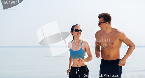 Image of couple in sports clothes running along on beach