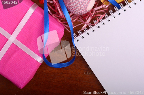 Image of Arrangement of Gift Boxes in Wrapping Paper with Checkered Ribbons and Decorated Easter Eggs. White paper notepad