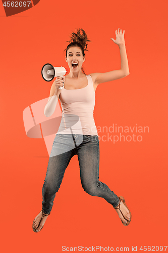 Image of Beautiful young woman jumping with megaphone isolated over red background