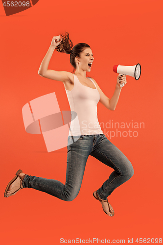 Image of Beautiful young woman jumping with megaphone isolated over red background