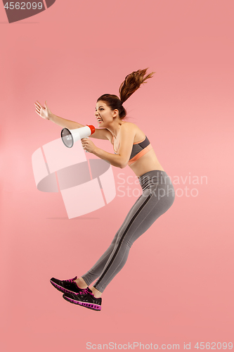Image of Beautiful young woman jumping with megaphone isolated over red background