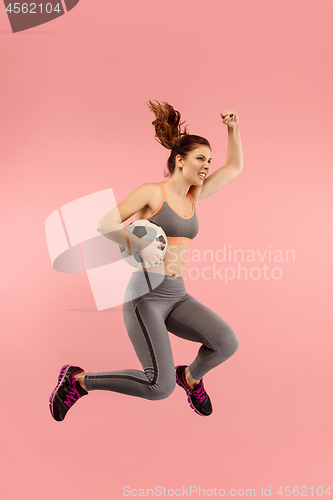 Image of Forward to the victory.The young woman as soccer football player jumping and kicking the ball at studio on a red