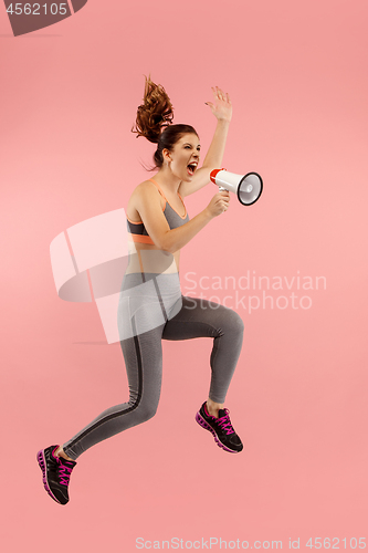 Image of Beautiful young woman jumping with megaphone isolated over red background