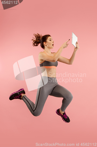Image of Image of young woman over blue background using laptop computer or tablet gadget while jumping.